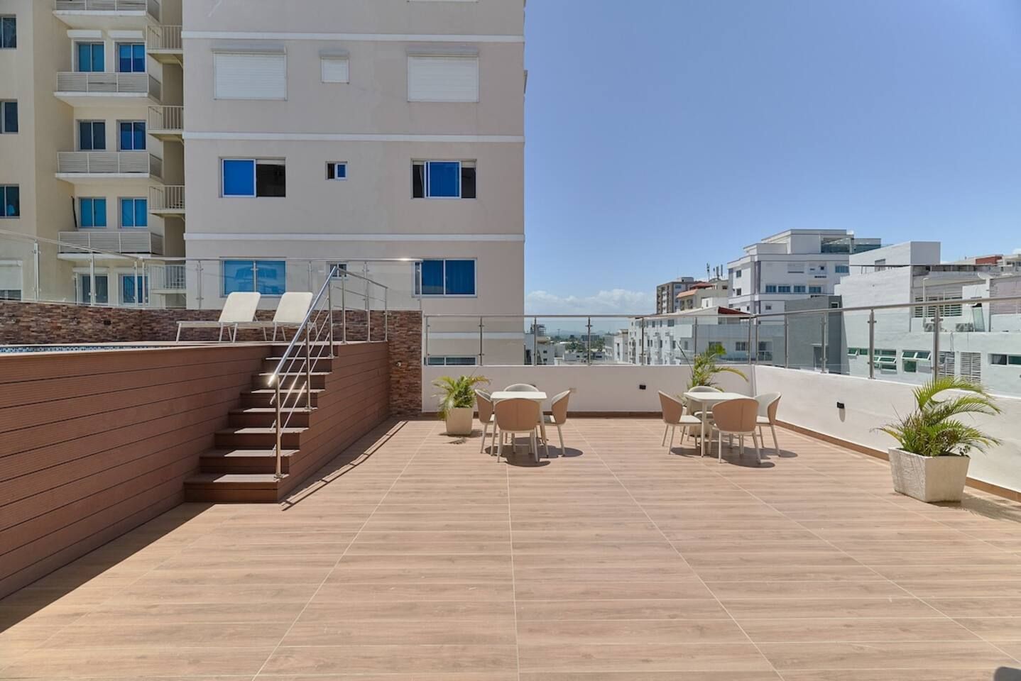 A rooftop terrace with a wooden staircase, outdoor seating, and a view of surrounding buildings.