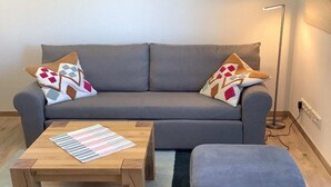 A grey sofa with patterned cushions, a striped table, and a small ottoman. - Ferienwohnung in Burhave (Burhave)