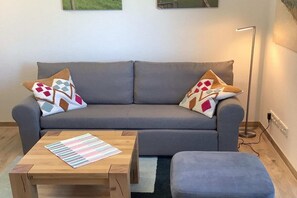 Ein graues Sofa mit gemusterten Kissen, ein gestreifter Tisch und ein kleiner Hocker.