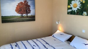 A bedroom with a bed, two pillows, a wall-mounted light, and two paintings. - Ferienwohnung in Burhave (Burhave)