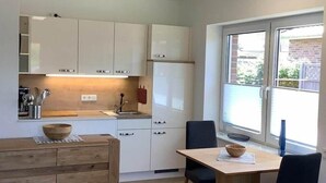 A modern kitchen with white cabinets, a wooden island, and a dining area with two chairs. - Ferienwohnung in Burhave (Burhave)