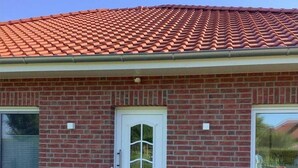 A brick house with a red-tiled roof, a white front door, and a small front yard with grass and a brick pathway. - Ferienwohnung in Burhave (Burhave)