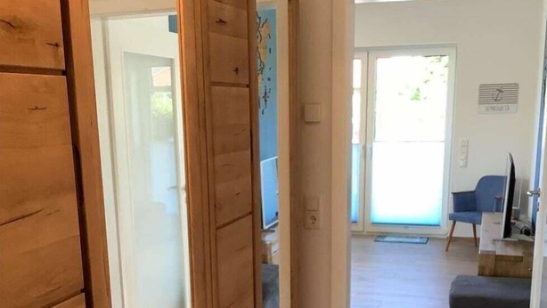 A wooden wardrobe with sliding doors, a grey sofa, and a television in a living room area. - Ferienwohnung in Burhave (Burhave)