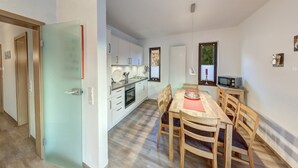 A modern kitchen with white cabinets, a dining table with chairs, and a microwave. - Großzügige Ferienwohnung für bis zu 9 Personen (Burhave)