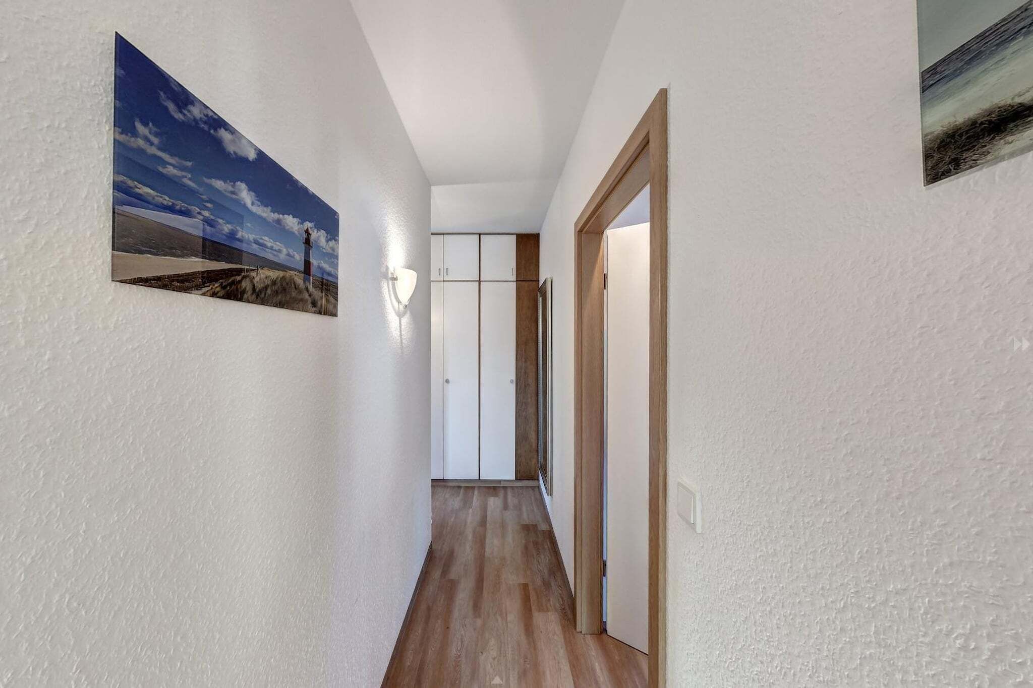 Ein Flur mit Holzboden, weißen Wänden und einer Tür zu einem Raum mit einem weißen Kleiderschrank und einem Spiegel.