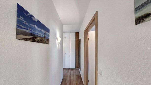 A hallway with a wooden floor, white walls, and a door leading to a room with a white wardrobe and a mirror. - Großzügige Ferienwohnung für bis zu 9 Personen (Burhave)
