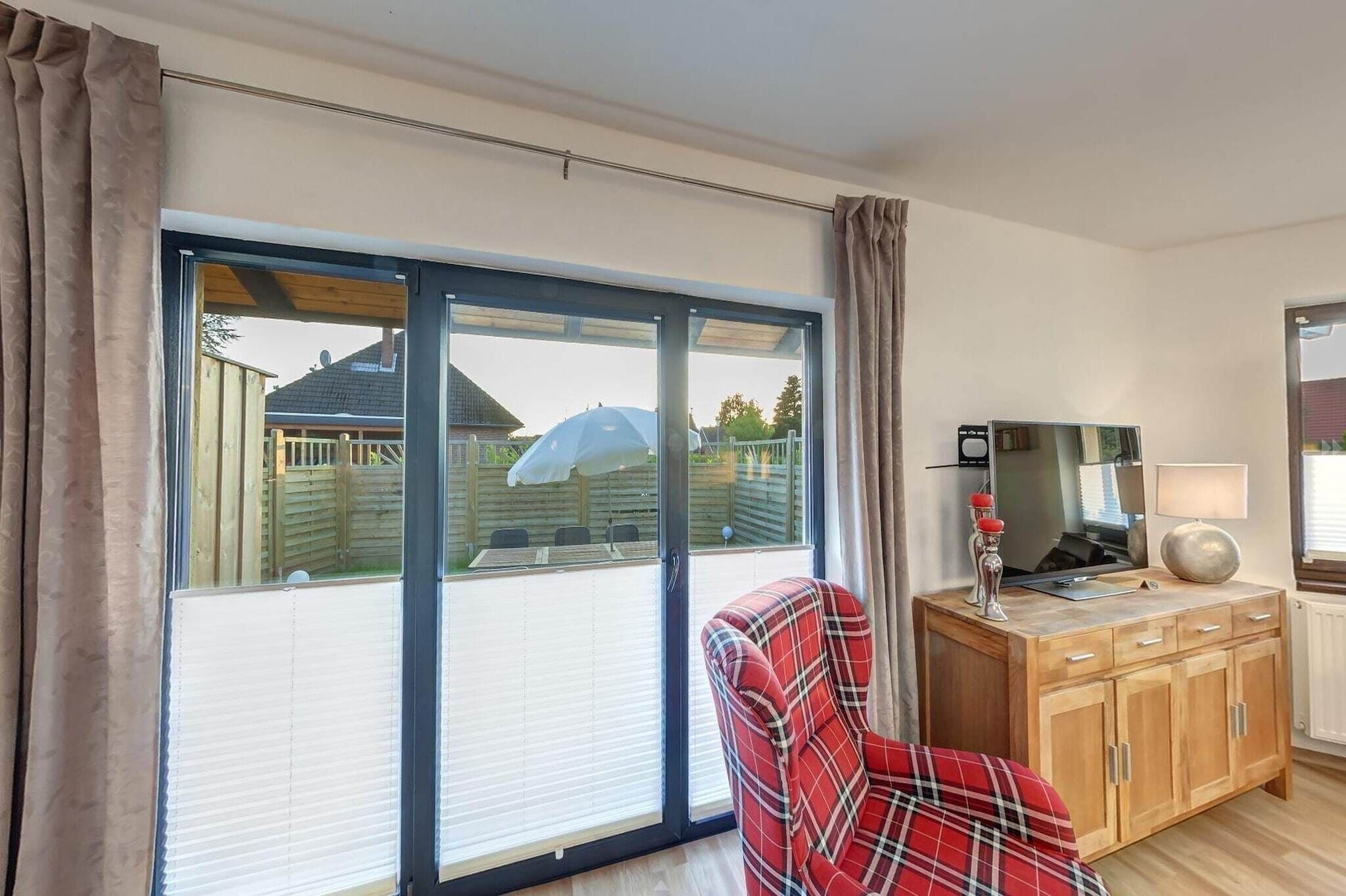 A room with a large sliding glass door leading to a covered outdoor area, a television on a wooden cabinet, and a plaid chair.