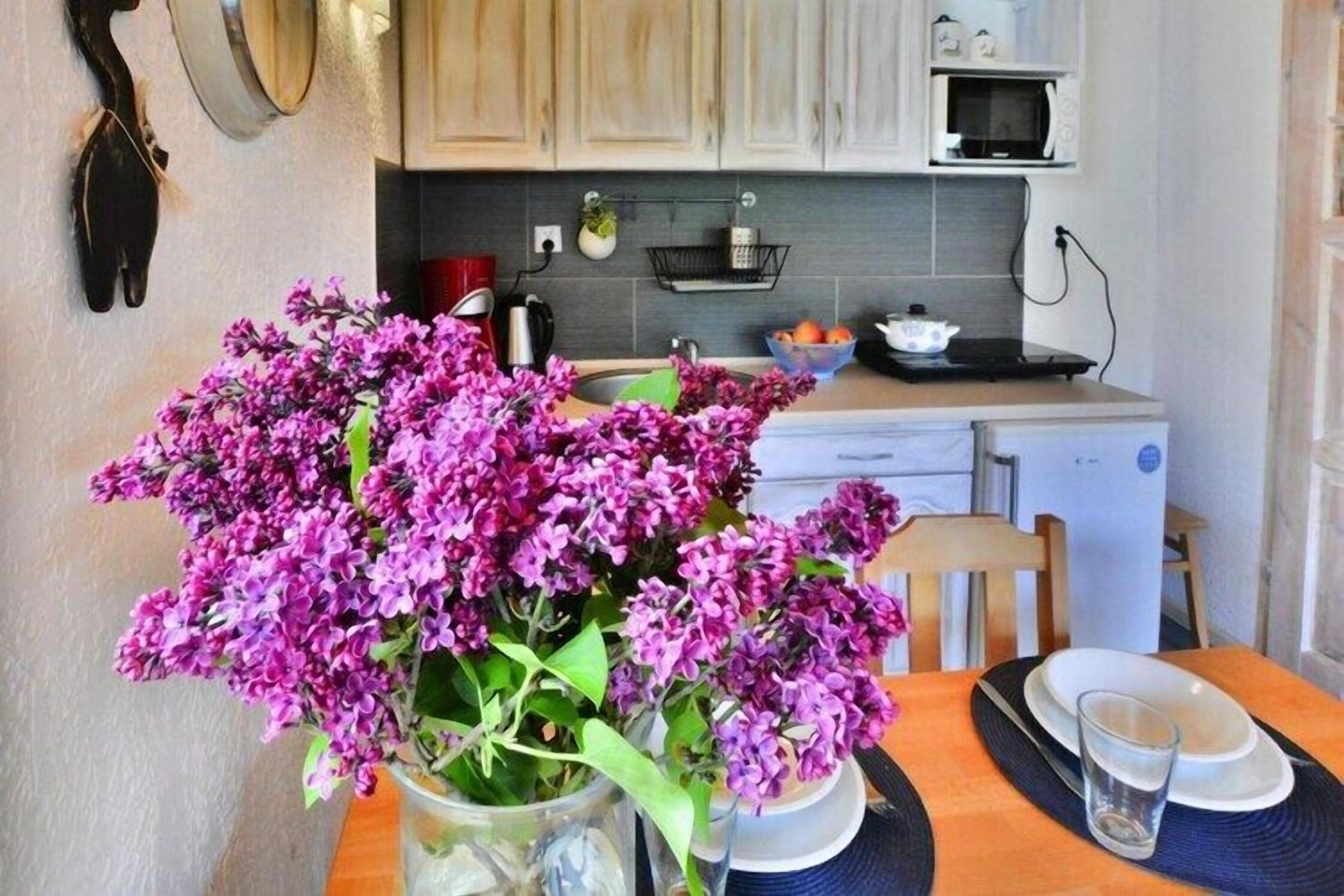 Une cuisine avec un vase de fleurs violettes sur la table, un four à micro-ondes et des placards.