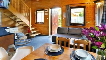 L’intérieur chaleureux d’un chalet avec un escalier en bois, un canapé, une table à manger dressée avec des assiettes et des verres, et un téléviseur fixé au mur.