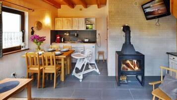 Une cuisine chaleureuse avec des meubles de rangement en bois, une table à manger avec des chaises, un petit tabouret et un poêle à bois noir.