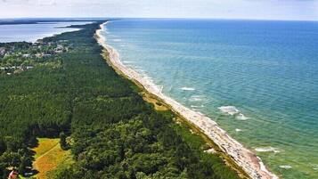 Une vue aérienne d’une zone côtière, avec une longue étendue de plage, une forêt dense et un petit village dont on aperçoit les bâtiments.
