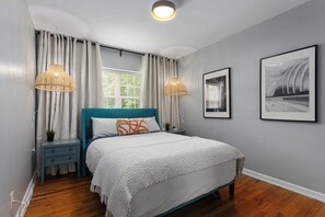 Quarto com cabeceira azul-turquesa, colcha branca e duas luminárias fixadas na parede.