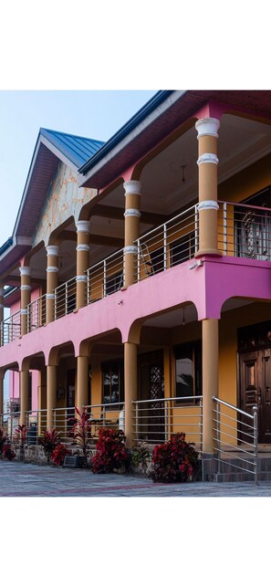 A building with a pink facade, multiple balconies, and a staircase leading to the entrance. - 2-bedroom apartment in soothing Prampram with cool AC and gym access (Prampram)