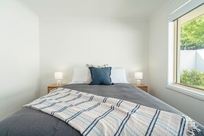 A neatly made bed with a striped blanket, two bedside lamps, and a window with a view of greenery. - Scenic Sandy Bay Lookout in the Hills (Sandy Bay)