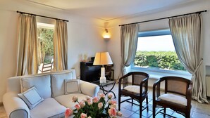 Ein Wohnzimmer mit Sofa, Sesseln, einer Lampe und Blick auf Grün durch große Fenster.
