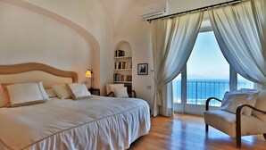 Ein Schlafzimmer mit einem großen Bett, einem Sessel, einem Bücherregal und Meerblick.