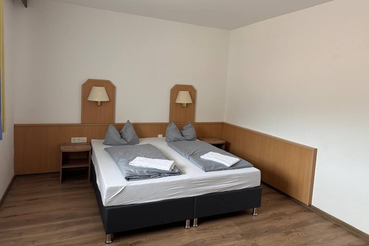 A double bed with grey bedding and pillows, two bedside tables with lamps, and a wooden headboard.