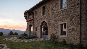 Un bâtiment en pierre, avec un chemin en pierre menant à l’entrée, entouré de pelouse et de petites plantes.