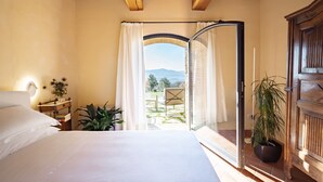 Une chambre à coucher avec un lit, une table de chevet avec une lampe, une plante en pot et une vue sur l’extérieur grâce à une porte vitrée.