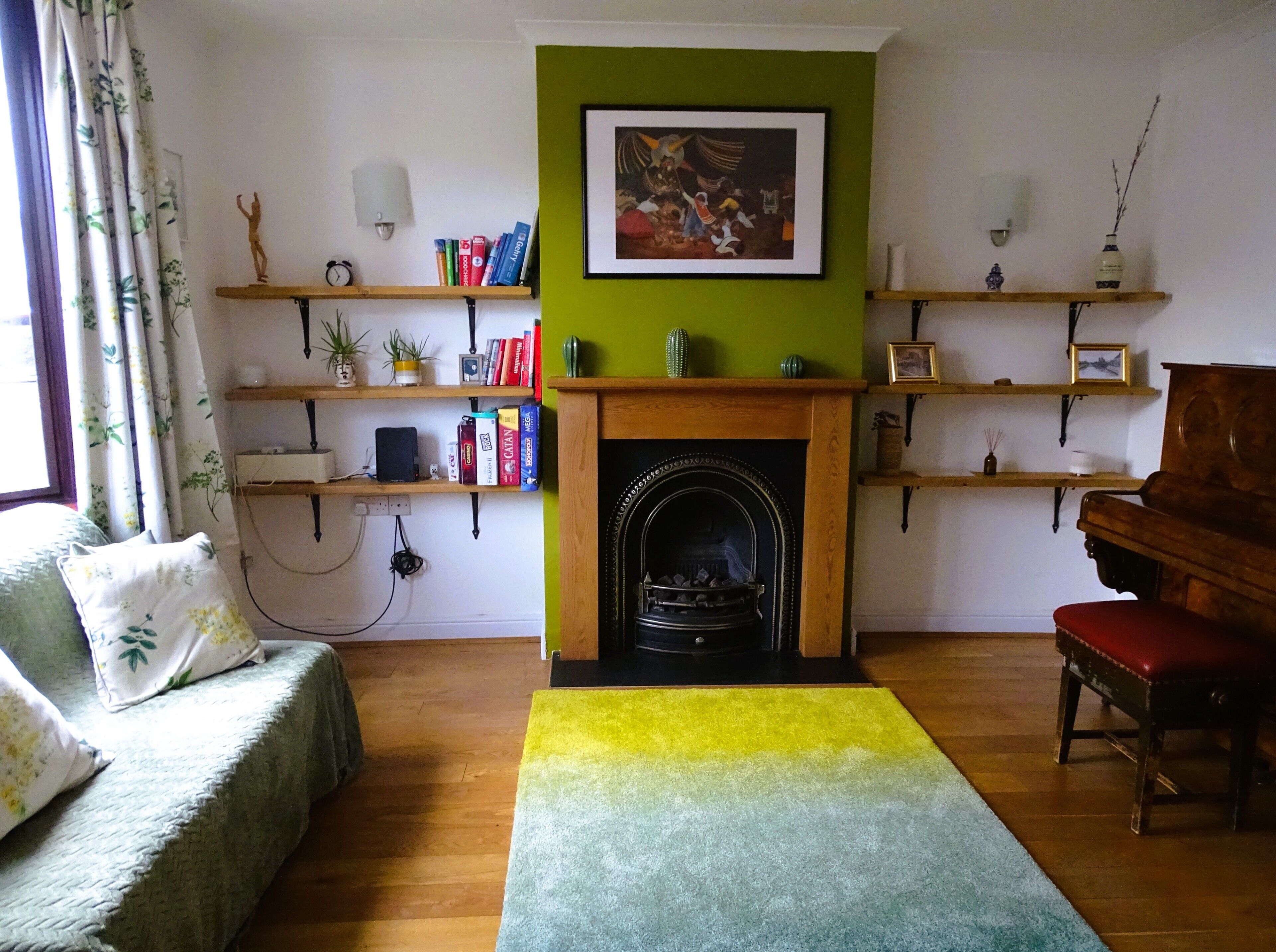 A living room with a fireplace, bookshelves, a sofa, a piano, and a colorful rug.