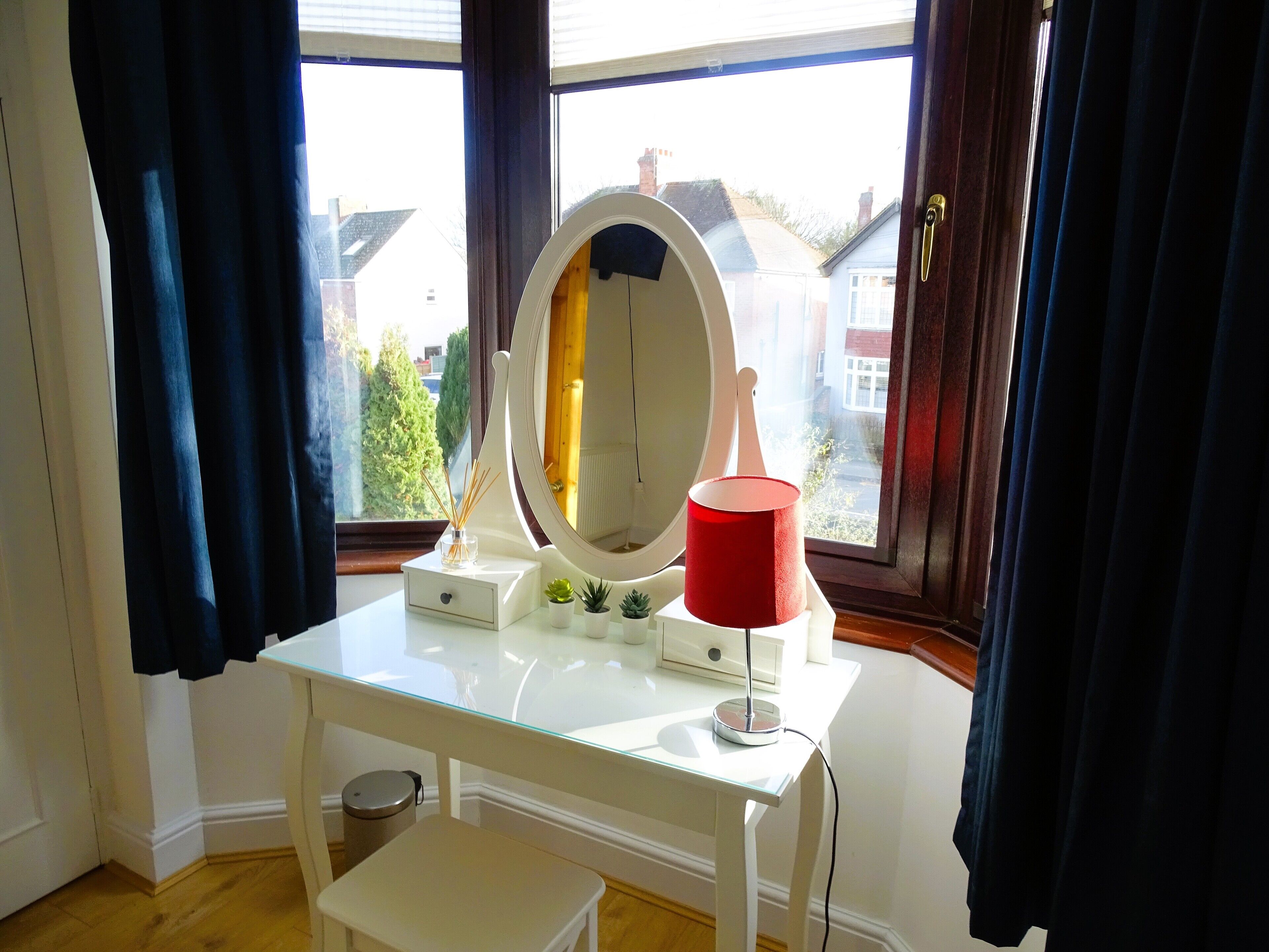A white vanity with a mirror, a red lamp, and a small plant.