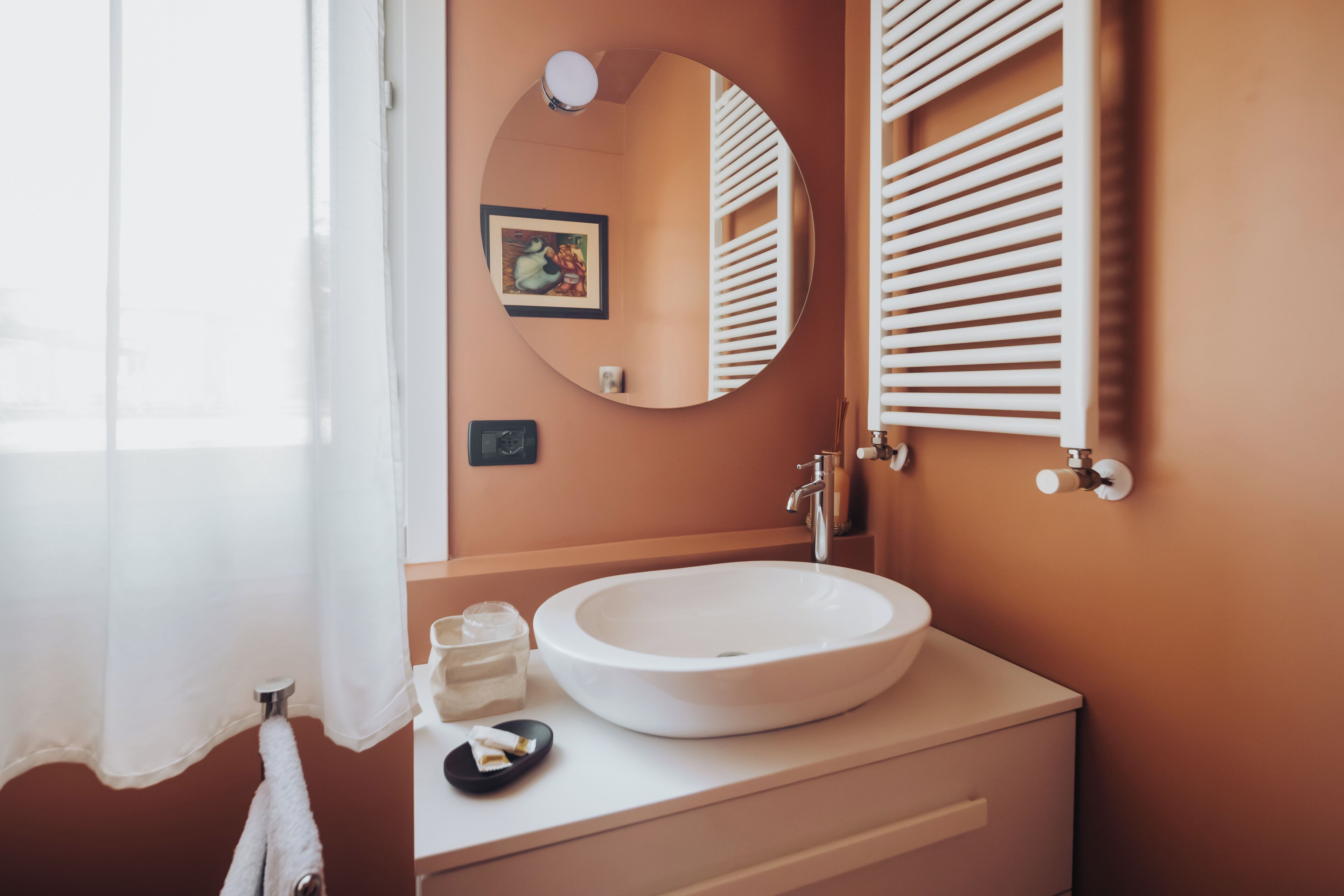 A bathroom with a round white sink, a mirror, and a towel rack.