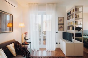 A living room with a sofa, a coffee table with a plant, a lamp, a television on a stand, and a bookshelf. - Romantic House   (Bologna)