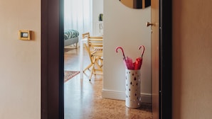 Un pasillo que da a una sala de estar con una mesa de comedor y sillas, un espejo y un jarrón decorativo con un paraguas rojo.