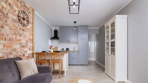 A modern kitchen with grey cabinets, a brick wall, and a dining area with a grey sofa and wooden table. - Modern Apartment | 2 Bedrooms | Workspace | Katowice. (Katowice)