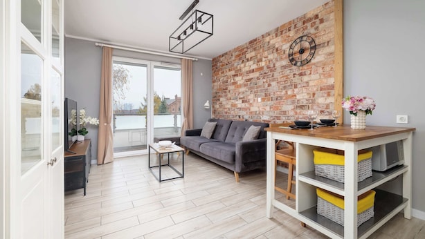 A modern living room with a grey sofa, a wooden coffee table, and a brick accent wall. - Modern Apartment | 2 Bedrooms | Workspace | Katowice. (Katowice)