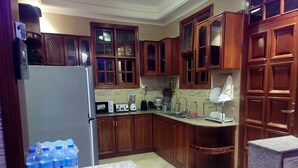 A kitchen with wooden cabinets, a refrigerator, a microwave, a toaster, a blender, and a sink. - Cape Villa (Arusha)