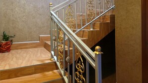 A wooden staircase with ornate metal railings and a potted plant on the landing. - Cape Villa (Arusha)