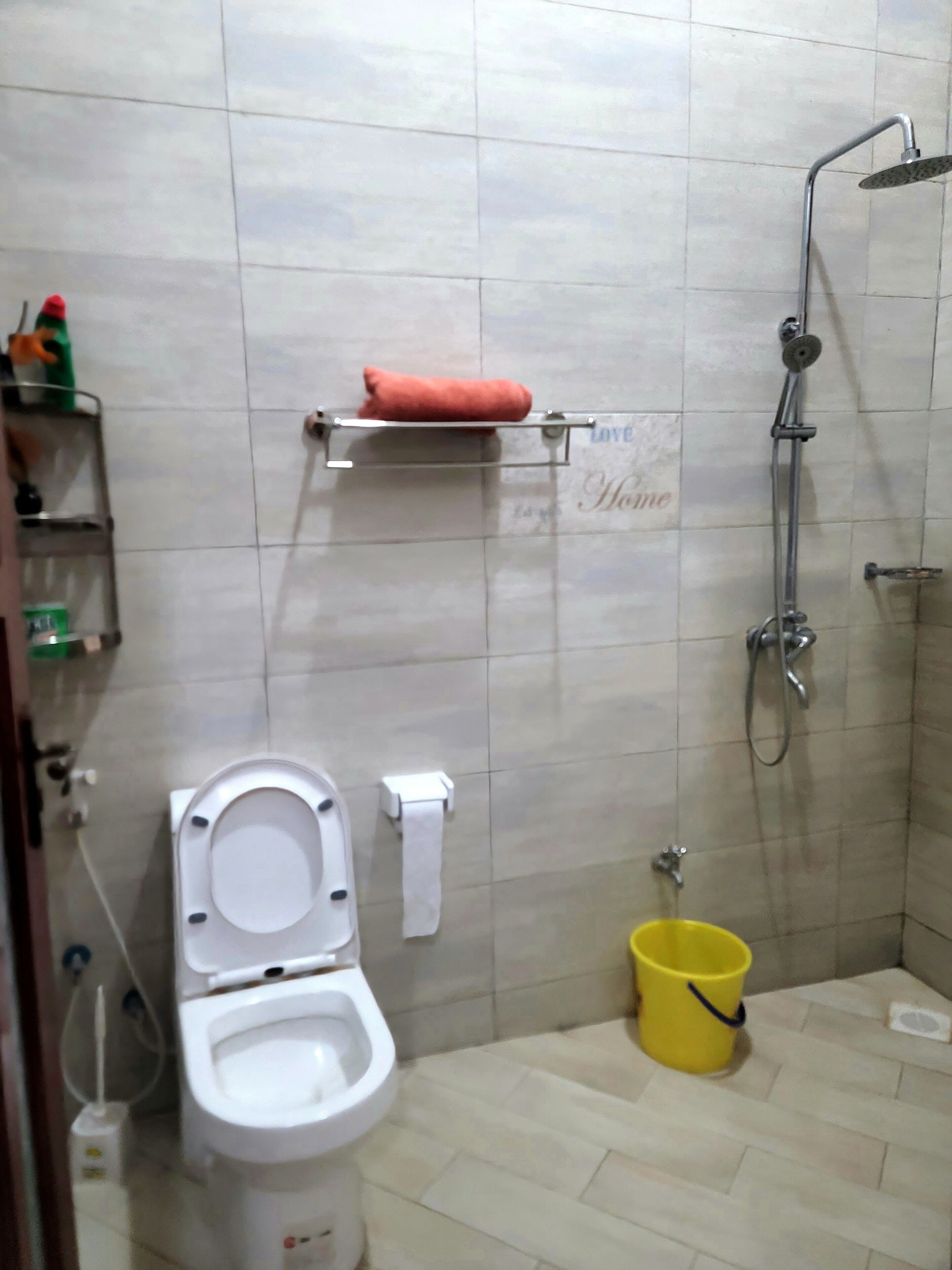 A bathroom with a toilet, a shower, and a yellow bucket on the floor.