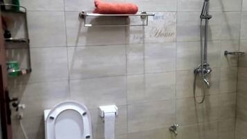 A bathroom with a toilet, a shower, and a yellow bucket on the floor.