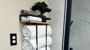 Ett badrum med en vägg av marmor, en duschdörr av glas och en handdukshängare med prydligt hoprullade handdukar och en liten krukväxt.