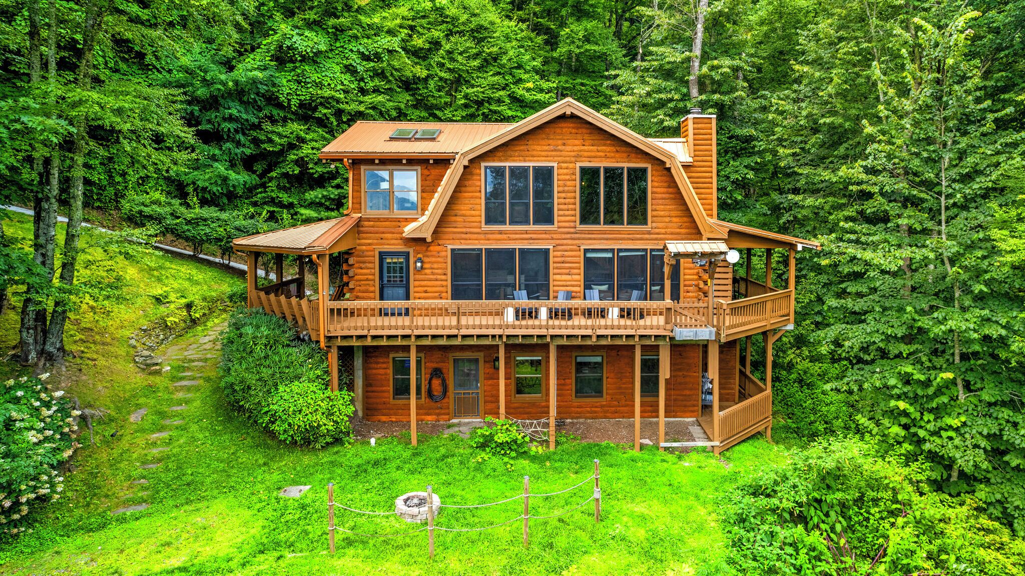 A two-story log cabin with a balcony, surrounded by dense forest.