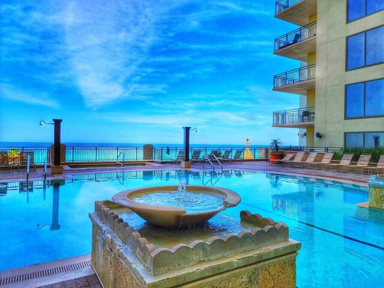 Ein Pool mit einer Fontäne, Liegestühlen und Blick auf den Ozean.