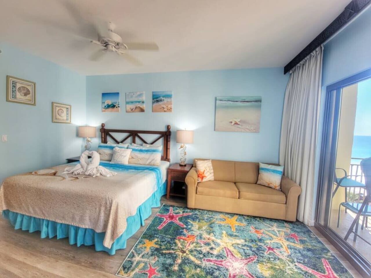 A bedroom with a bed, a sofa, a starfish-patterned rug, and a ceiling fan.