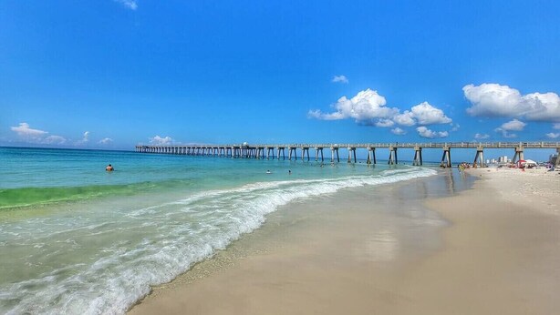Une plage avec une jetée qui s’avance dans l’océan, un ciel dégagé et une eau calme.