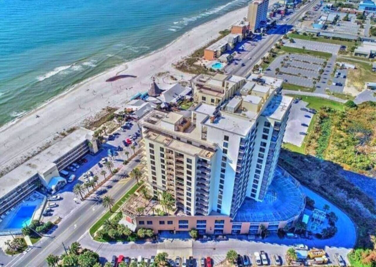 Vista aérea de un hotel costero con varias construcciones, una playa y un estacionamiento.