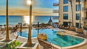 Une piscine d’hôtel avec vue sur l’océan, des palmiers et un immeuble doté de balcons.