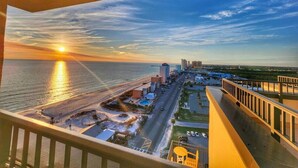 Un balcon offrant une vue sur une plage et sur le paysage urbain au coucher du soleil.