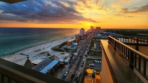 A coastal cityscape with a sunset over the ocean, buildings, and a road leading to the beach. - Balcony | Walk to Pier Park | Beach Across Street (Panama City Beach)