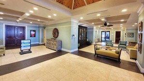 A spacious lobby with a high ceiling, a reception desk, seating area, and a large wall clock. - Balcony | Walk to Pier Park | Beach Across Street (Panama City Beach)
