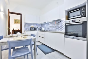 A modern kitchen with white cabinets, a blue and white tiled backsplash, a built-in oven, and a dining area with a table and chairs. - Bright apartment with a balcony overlooking Viale Augusto, in the heart of Fuorigrotta, in an elegant, recently renovated building with concierge service. The location is very convenient for reaching the historic center, the seafront, or Pozzuoli: the Me (Naples)