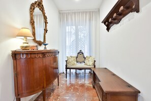 A room with a wooden cabinet, a lamp, a mirror, a bench with cushions, and a wooden chest of drawers. - GuestHost - Partenope Stadium House (Naples)