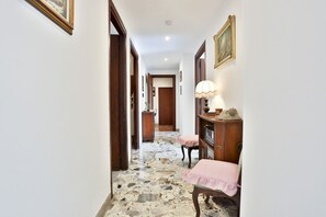 A hallway with a stone floor, wooden doors, and a desk with a lamp. - GuestHost - Partenope Stadium House (Naples)