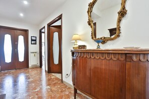 A hallway with wooden doors, a marble floor, a wooden cabinet with a mirror, and a lamp. - Bright apartment with a balcony overlooking Viale Augusto, in the heart of Fuorigrotta, in an elegant, recently renovated building with concierge service. The location is very convenient for reaching the historic center, the seafront, or Pozzuoli: the Me (Naples)