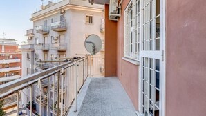 Ein schmaler Balkon mit Metallgeländer, einer Satellitenschüssel und einem Fenster mit weißen Rahmen.