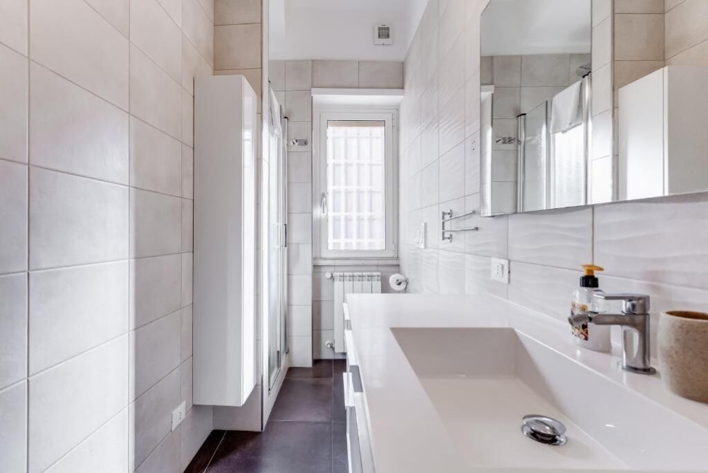 A modern bathroom with a large white sink, a mirror, and a window.
